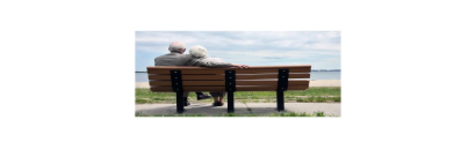 An elderly couple sitting closely together on a bench looking at the water.