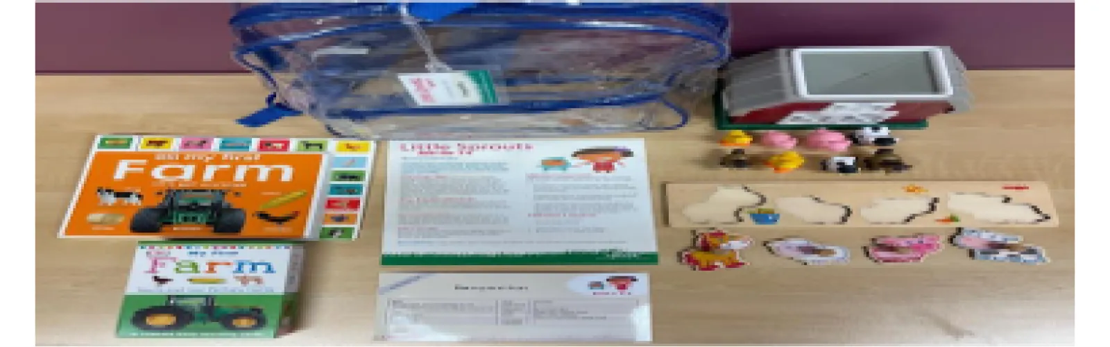 A clear backpack displayed with 2 books, some laminated instruction and activity sheets, a barn with animals, and a wooden puzzle.